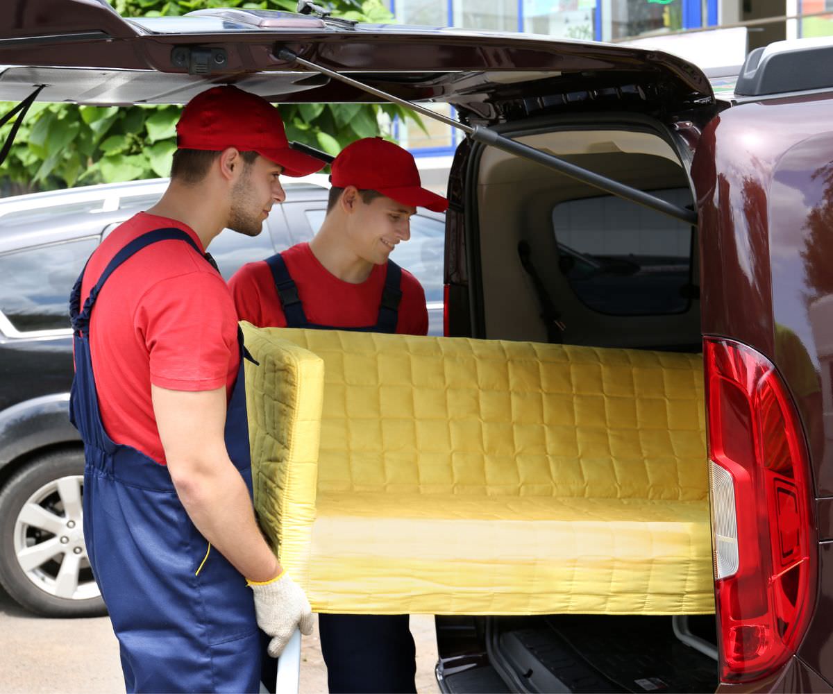 Umzugshelfer laden ein gelbes Sofa in einen Transporter – Umzugskosten sparen