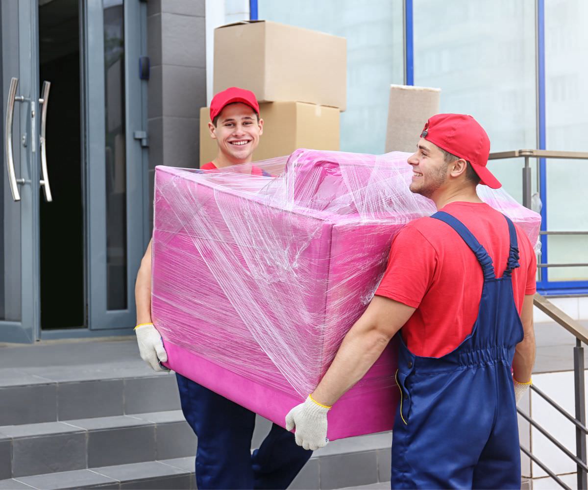 Umzugsfirma: Zwei Umzugshelfer tragen ein in Folie gepacktes Möbelstück