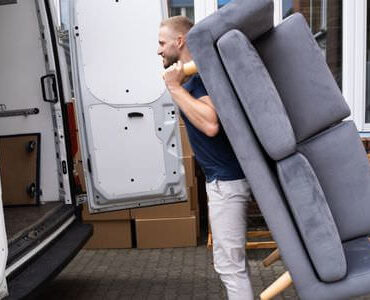 Möbellift Zwickau: Helfer tragen ein graues Sofa aus einem Transporter
